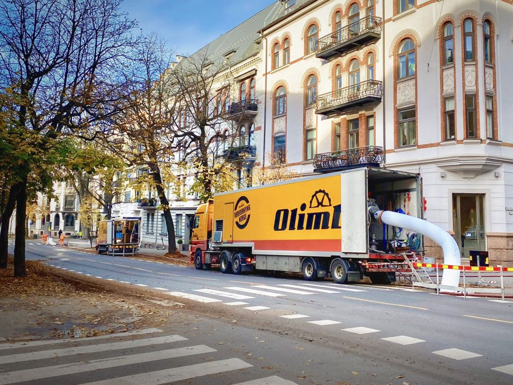 Olimb-lastebil parkert langs Bygdøy allé i Oslo, med en hvit strømpe ført fra bilen ned til gaten foran en eldre bygård, under strømperenovering.